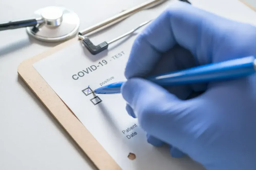 Person wearing gloves marking down a positive result from a COVID-19 test on a clip board
